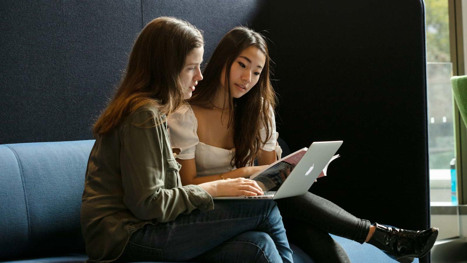 两个学生坐在高靠背的沙发上，用笔记本电脑学习 
